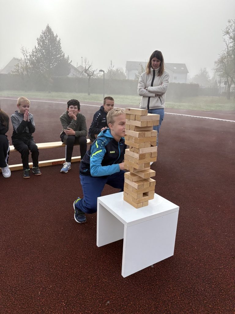 Ein Schüler zieht einen Stein aus einem Jenga- Turm, andere schauen zu